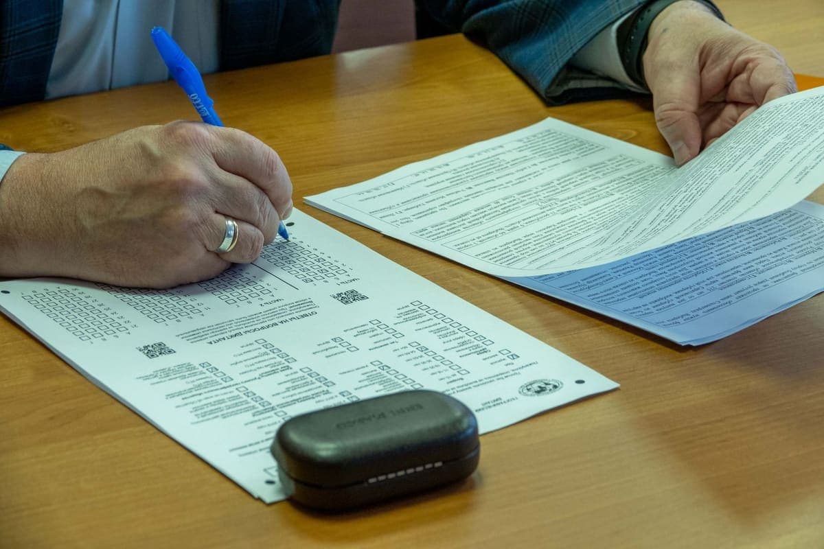Close-up of a person filling out official documents with a pen at a wooden desk