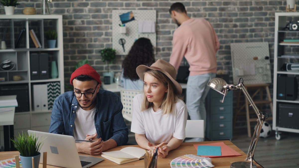 Small team working at desks in a bright open-plan office with supply shelves