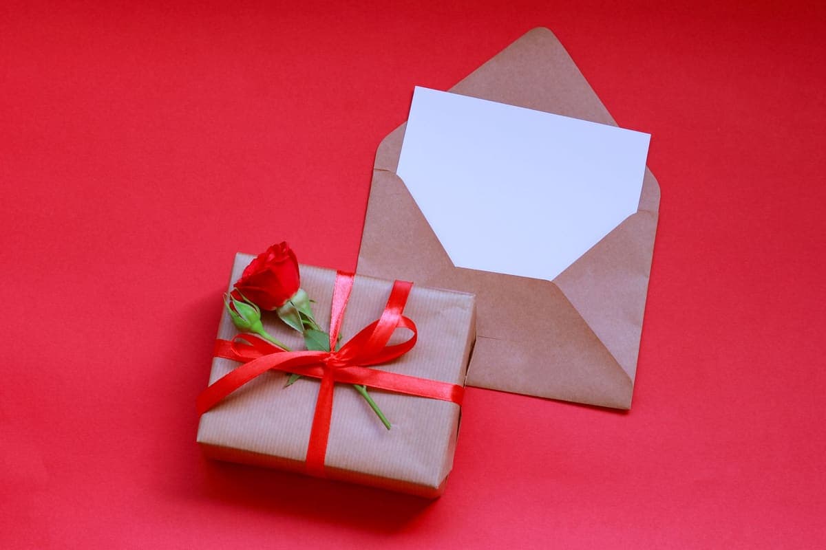 Gift box with a rose and an envelope arranged on a red background