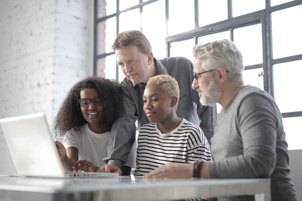 Group of colleagues in casual clothing gathered around a laptop in an office
