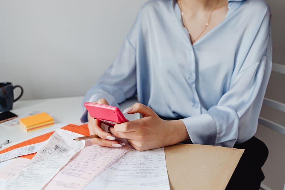 Person using a calculator at a desk covered with bills and receipts