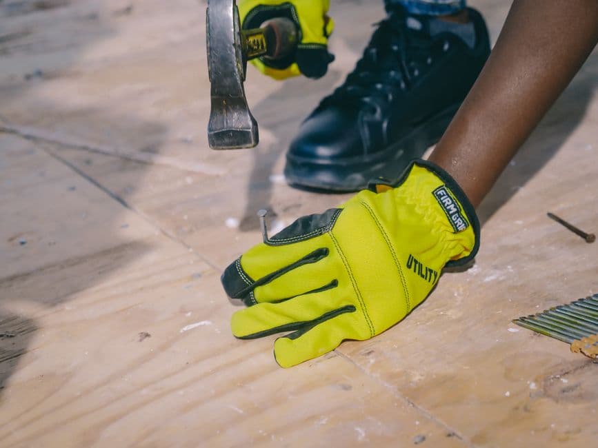 Gloved hands hammering a nail into a wooden surface on a workbench