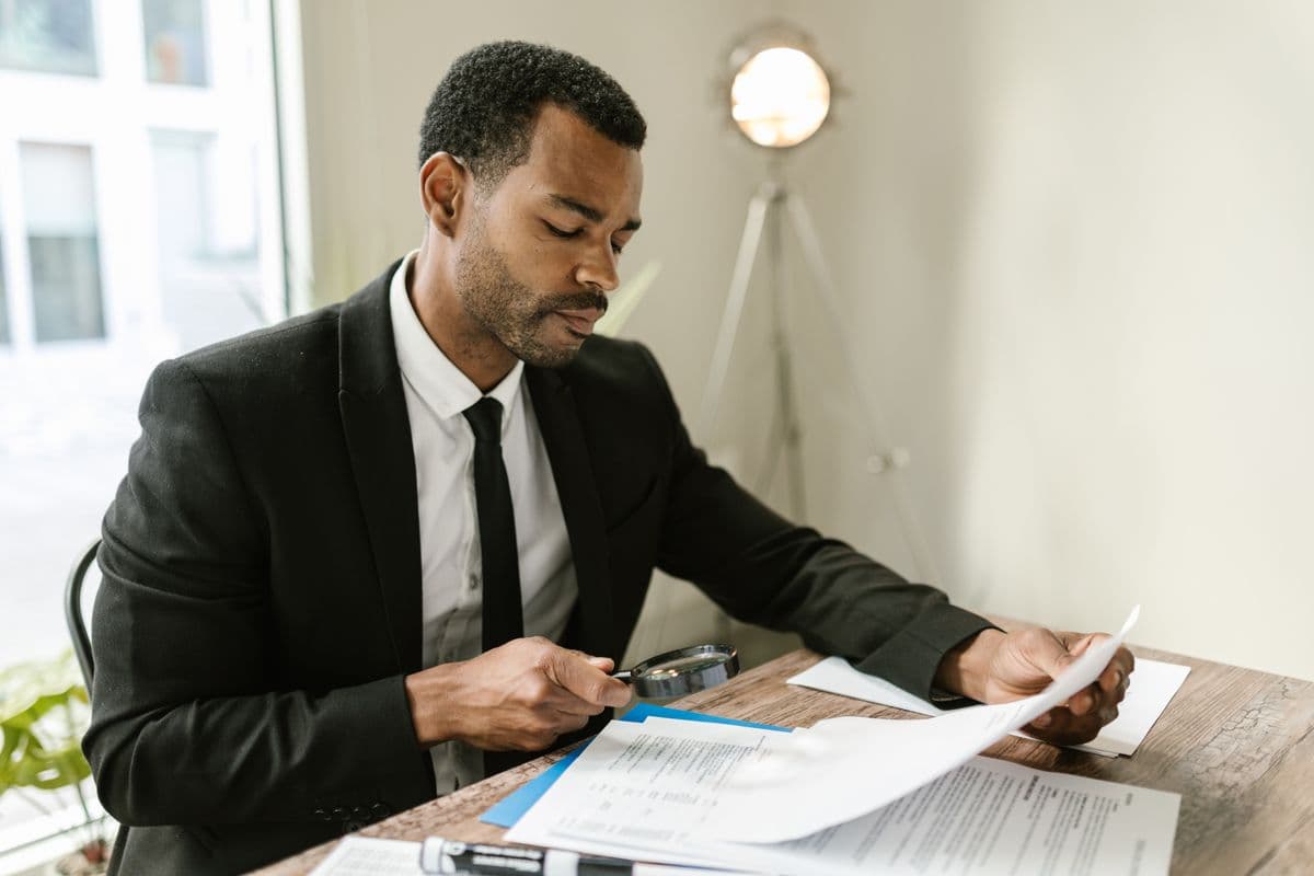 Person examining a paper document closely with a magnifying glass at an office desk