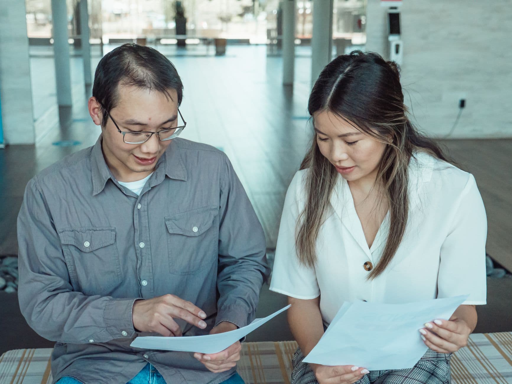 Two colleagues comparing paperwork across a desk in a small office