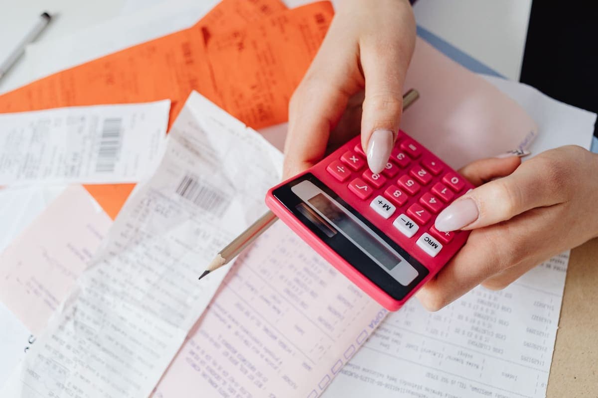 Hands using a calculator to total expenses among scattered paper receipts